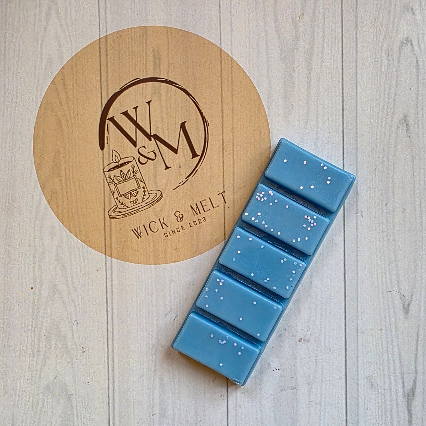 Blue wax melts on a wooden coaster with a brand logo on a light wooden surface