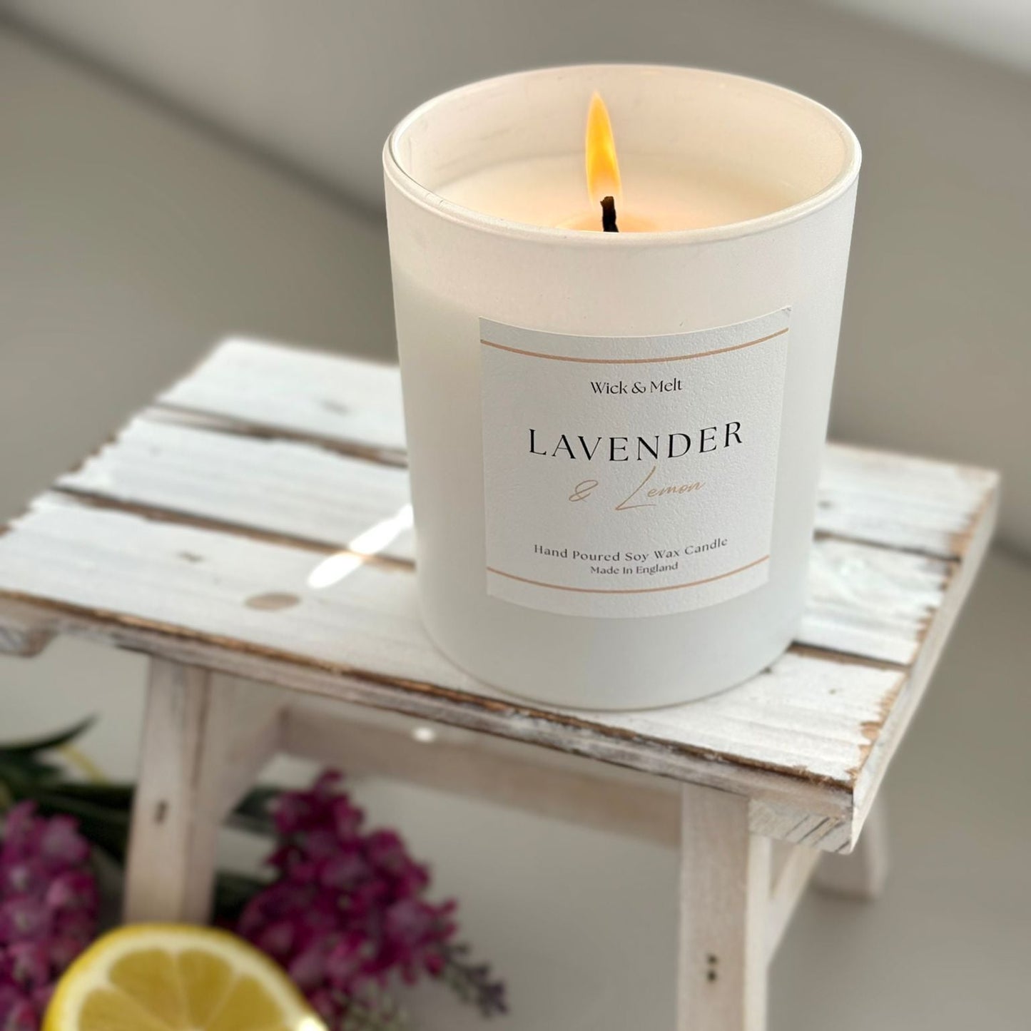Lavender and lemon candle on a wooden stand with lemons and flowers in the background