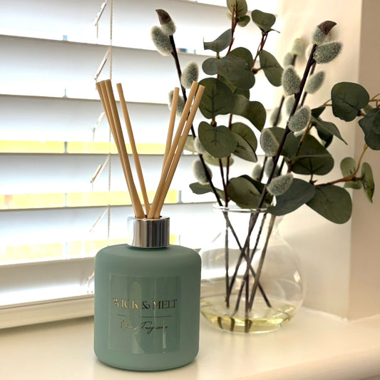 Green diffuser bottle with wooden sticks and eucalyptus branches on a windowsill.