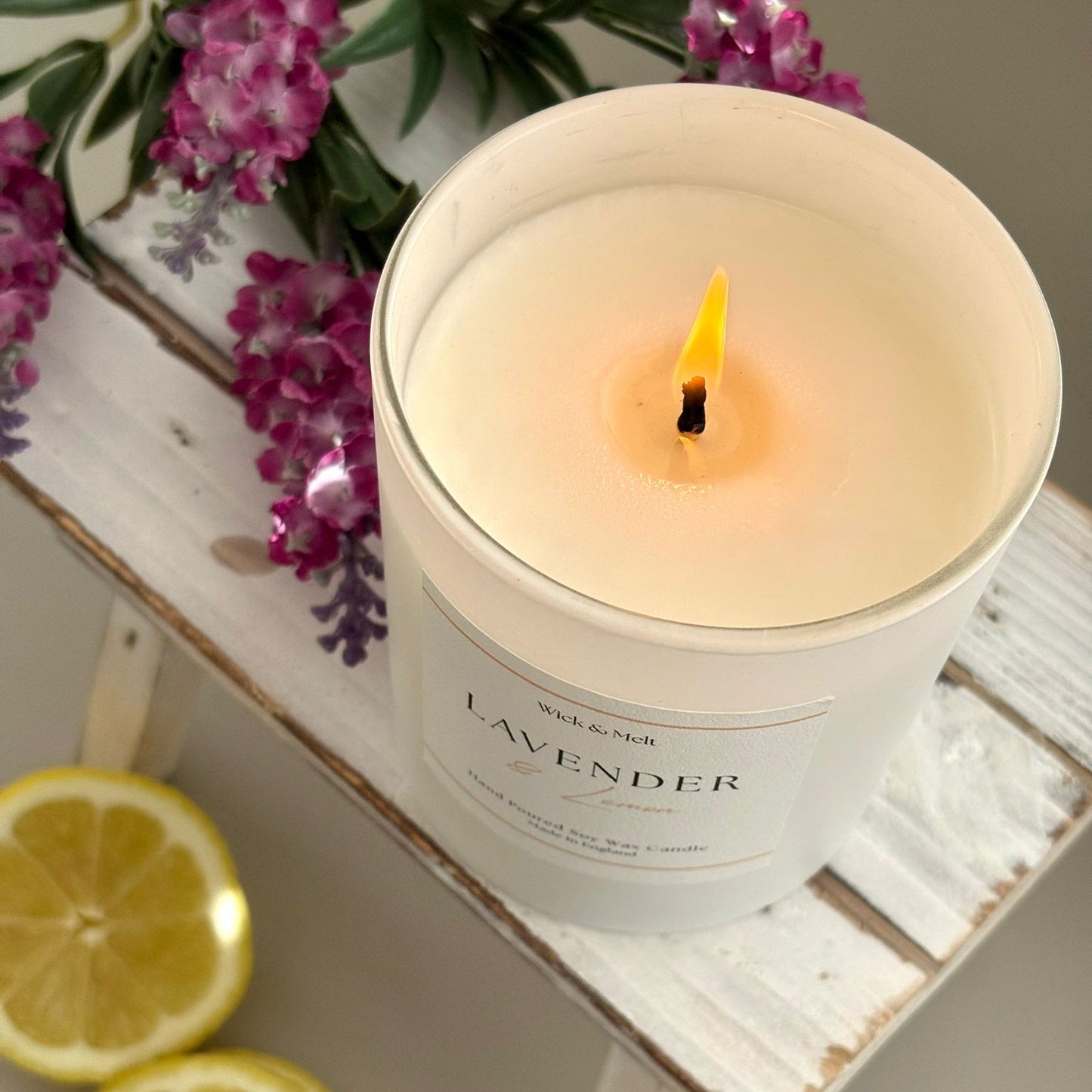 Lavender candle on a small wooden table with lemons and lavender flowers.